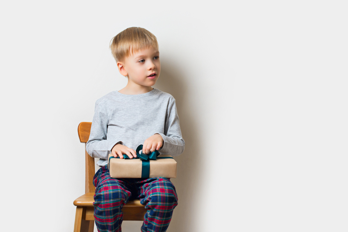 Scandinavian lifestyle minimalism christmas and new year concept with kid - little boy with stack of gift box on a chair in room, white background