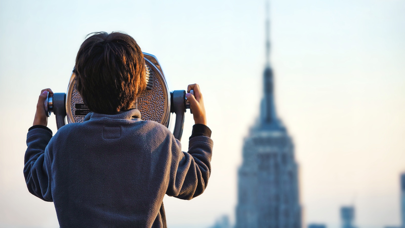 Child looks through binoculars at Empire State Building