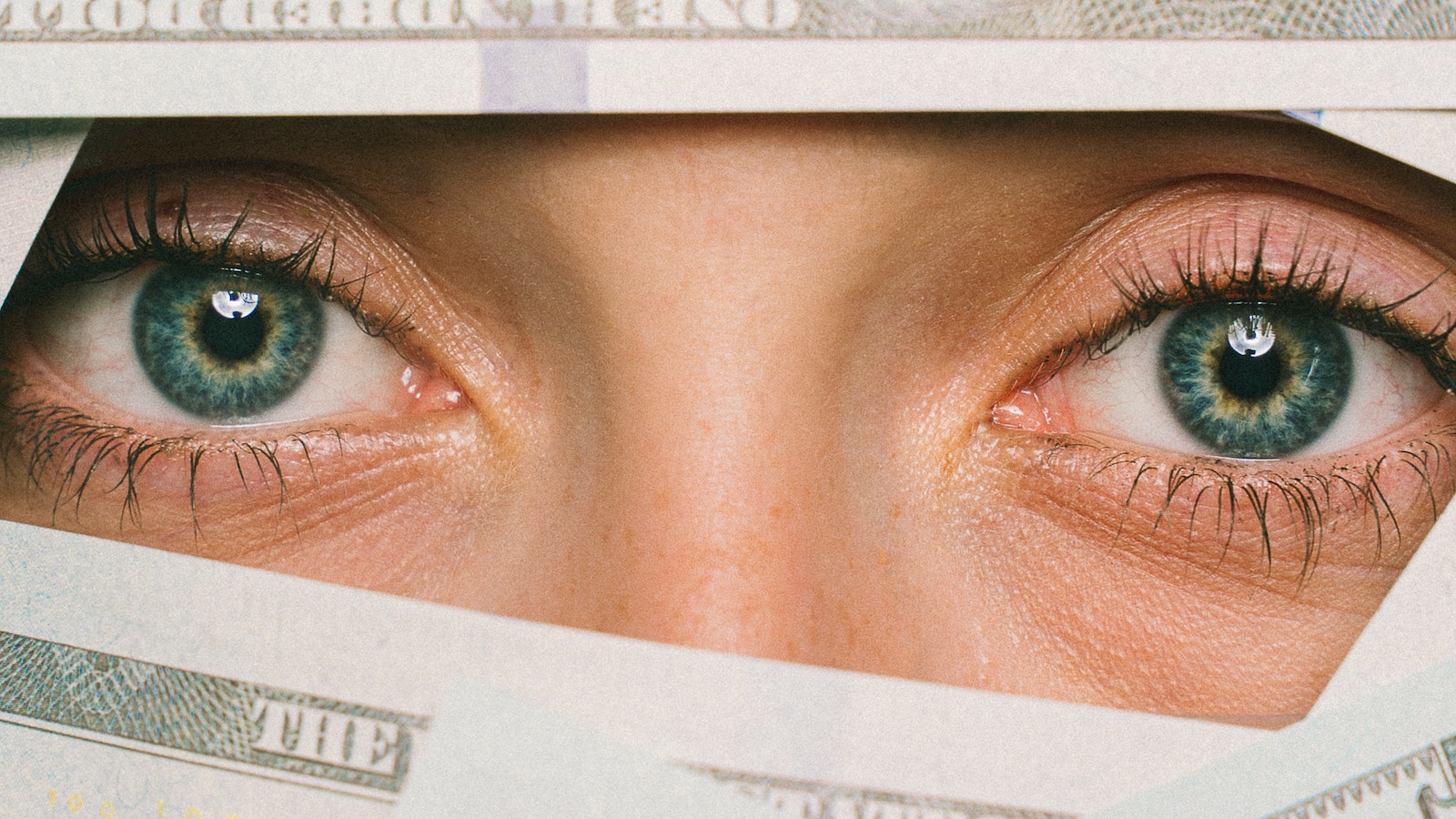 Woman eyes peeking through hundred dollar bills